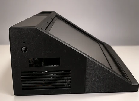 Lateral izquierdo del prototipo: carcasa negra en cuña con la pantalla inclinada, rejilla de ventilación y huecos en el lateral.